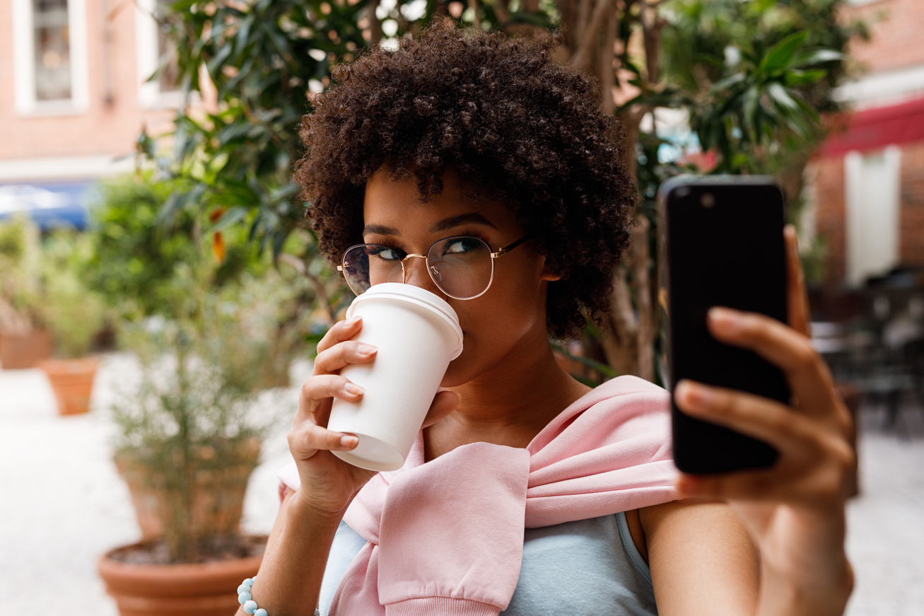 Female blogger taking a selfie on smartphone while drinking a coffee